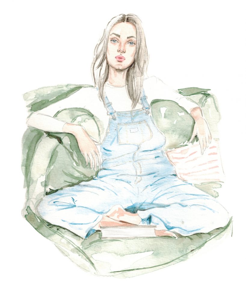 Frau mit langen Haaren sitzt auf einem grünen Sofa und trägt ein weißes Longsleeve und eine hellblaue Latzhose von levi´s und vor ihr liegt ein Buch
